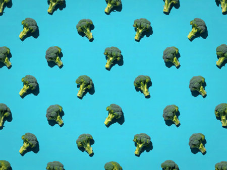 A repeating pattern of fresh broccoli florets arranged on a bright, solid blue surface, creating a...