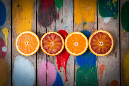 A top-down view of four orange slices, two regular and two blood oranges, arranged on a rustic...