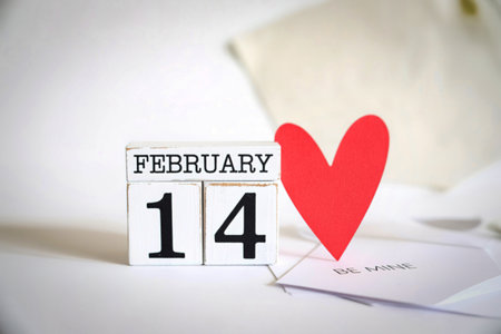 A rustic wooden block calendar displays February 14th next to a vibrant red heart and a card with the phrase 'Be Mine,' evoking Valentine's Day.の写真素材