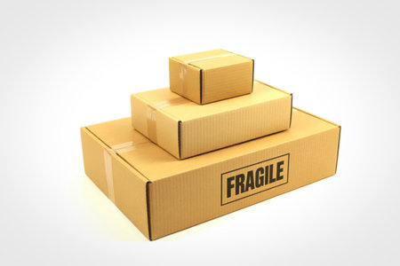 Three cardboard boxes of varying sizes are stacked on a white background. The largest box has a prominent 'Fragile' label.の写真素材