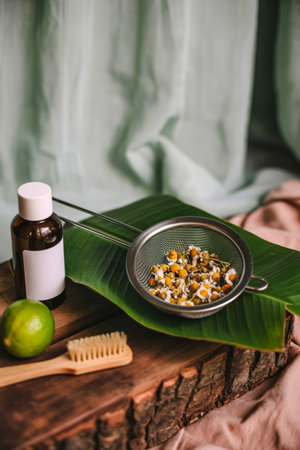 A still life featuring a lime, a small brush, a bottle, and a sieve with herbs on a banana leaf.の写真素材