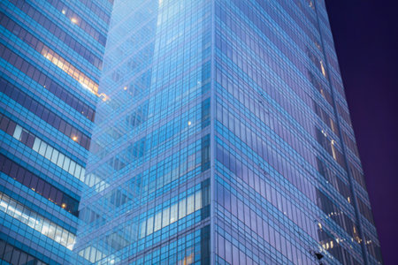 A towering glass skyscraper reflects city lights and the night sky, showcasing its sleek, contemporary architecture.の写真素材