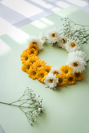 A delicate heart-shaped wreath crafted from vibrant yellow and white daisies, accented with wisps of...