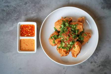 A white oval plate holds golden brown crispy chicken bites topped with chopped green herbs. Two dipping sauces are in a small white rectangular dish.の写真素材