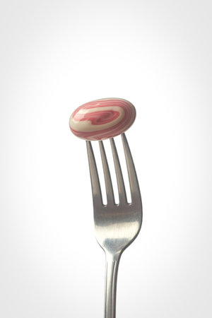 A close-up shot features a single, cooked sausage link skewered on the tines of a metal fork,...