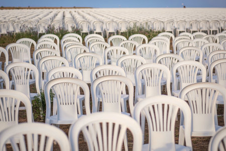 Numerous white plastic chairs are arranged in neat rows outdoors, suggesting a waiting area or an event setup.の写真素材