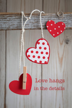 Three charming handmade hearts, two with red and white polka dots, hang suspended by twine against a rustic wooden background.の写真素材