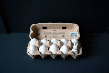 A carton of white eggs sits on a dark surface, with some eggs partially obscured by the carton's lid.の写真素材