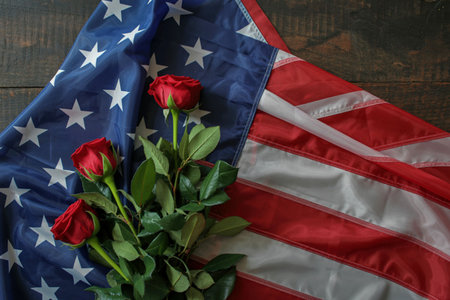 A close-up shot features three vibrant red roses with green stems and leaves resting on a weathered American flag.の写真素材