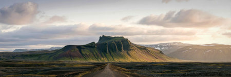 A panoramic view of a rugged mountain range with a winding dirt path leading towards the mountains....