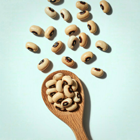 A wooden spoon filled with black-eyed peas, with additional peas scattered around it on a light...