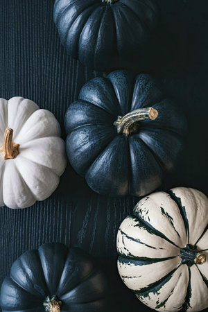 A collection of pumpkins in various colors and patterns arranged on a dark wooden surface. The...