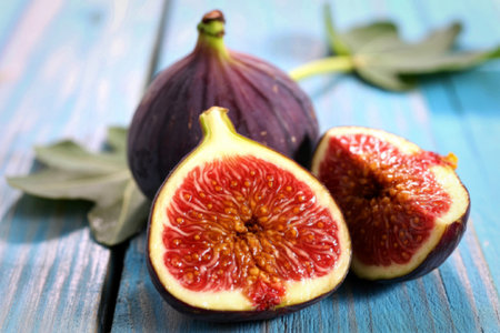 A close-up image of a whole fig and a sliced fig placed on a wooden surface, surrounded by a few...