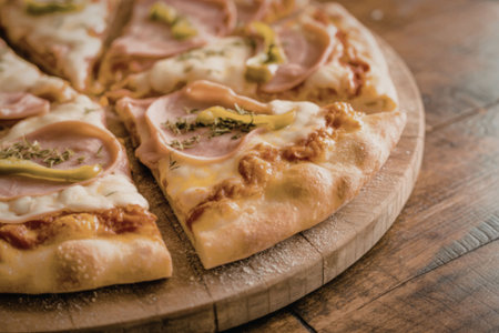 A close-up view of sliced pizza on a wooden board, topped with ham and cheese.の写真素材