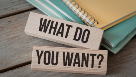 Two wooden blocks with the phrase 'what do you want' on a wooden desk accompanied by notebooksの写真素材