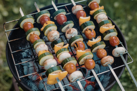 Colorful vegetable skewers with cherry tomatoes, mushrooms, zucchini, and bell peppers being grilled on a charcoal grill.の写真素材