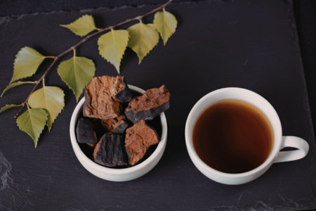 A cup of birch bark tea accompanied by dried birch bark pieces on a black slate surface, evoking a sense of natural remedy and traditional herbalism.の写真素材
