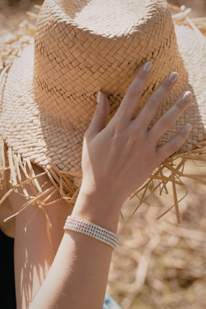 A woman is seen from behind, wearing a straw hat and a bracelet, standing in a field.の写真素材