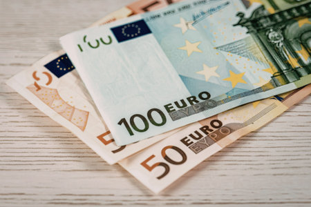 A close-up view of various euro banknotes arranged on a light-colored wooden surface, showcasing denominations of 50 and 100 euros.の写真素材