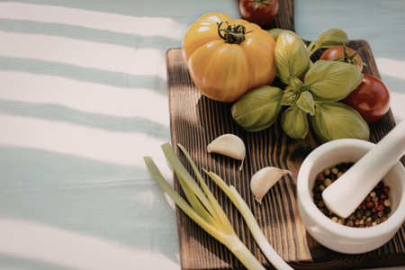 A wooden cutting board displays vibrant vegetables and a mortar with peppercorns, set against a white tablecloth with shadows.の写真素材