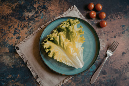 A plate of fresh lettuce leaves on a blue plate with a fork and cherry tomatoes on the side.の写真素材
