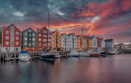a row of colorful houses by the water with boats docked in front of them under a vibrant sunset skyの写真素材
