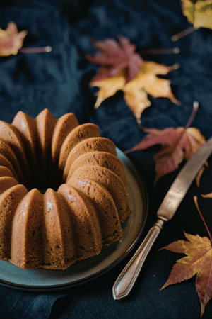 A brown bundt cake on a plate with a knife and autumn leavesの写真素材