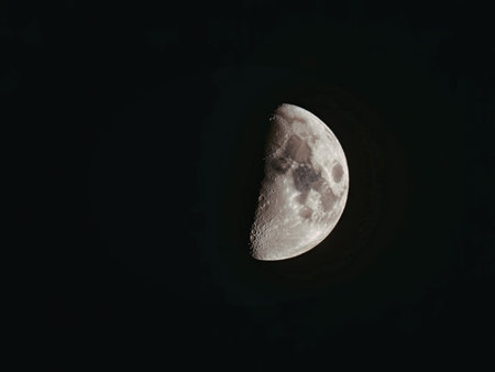 The image shows a half-illuminated moon against a black background, showcasing its cratered surface.の写真素材