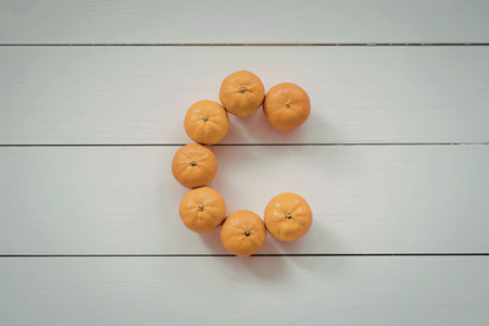 An arrangement of seven small oranges on a white wooden surface, possibly a table or floor, with the oranges forming a curved shape.の写真素材
