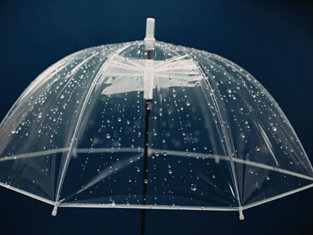 A clear plastic umbrella with raindrops on it, against a dark blue background.の写真素材