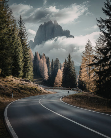 A scenic winding road cutting through a forest with evergreen trees and a mountain peak in the...