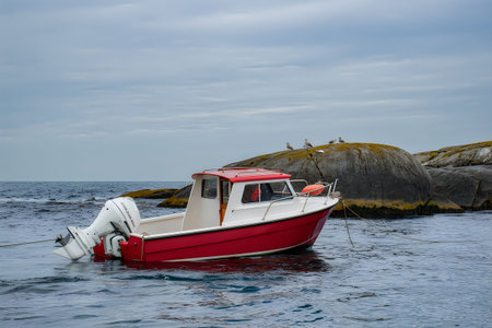 A small red and white boat floats on calm waters near a rocky shore.