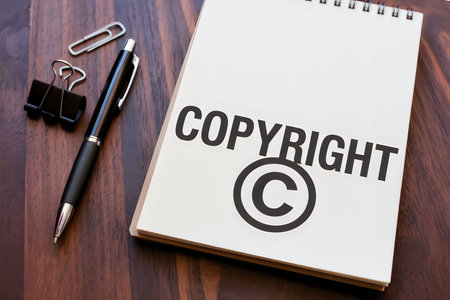 A spiral-bound notebook with a copyright symbol on a wooden desk with a pen and paperclip.の写真素材