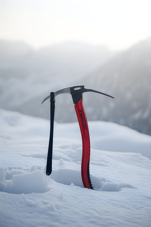 An ice axe stuck in the snow with a mountain range in the background.