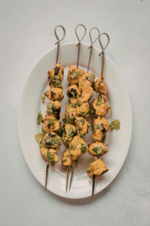 A plate of chicken tikka skewers garnished with green herbs, served on a white oval plate.