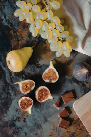 An arrangement of fresh fruits including grapes, pear, figs, and chocolate on a dark surface.の写真素材