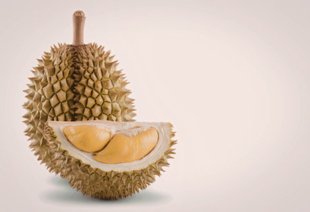 A durian fruit cut in half revealing its yellow flesh and spiky green skin on a white background