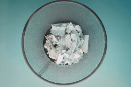 A glass bowl with a patterned design and a dark rim sits on a teal surface. The bowl contains crumpled white papers.
