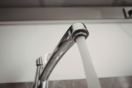 This image presents a detailed close-up of a faucet with water flowing from it, showcasing the shiny metal fixture and the stream of water.