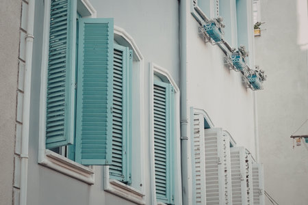The image depicts a building exterior with teal and white shutters on the windows. There are pipes and fixtures on the wall.