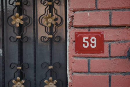 A red house number plate with the number 59 on a brick wall next to a black metal gate.
