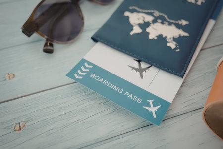 A blue travel wallet with a world map, a boarding pass, sunglasses, and a leather item on a light blue wooden table.