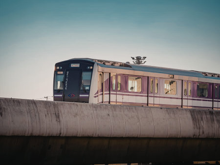 A purple and white train on a concrete bridge with a blue sky background