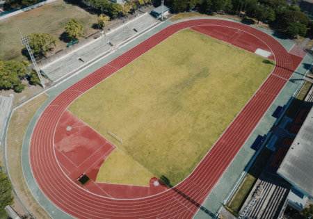 an aerial view of a red track and field stadium with a green grass field surrounded by a running track and bleachers on a sunny day