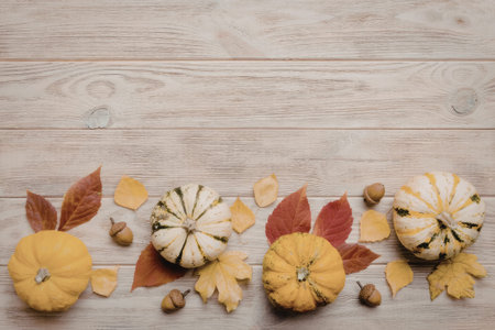 A row of small pumpkins and gourds arranged with autumn leaves and acorns on a wooden surface