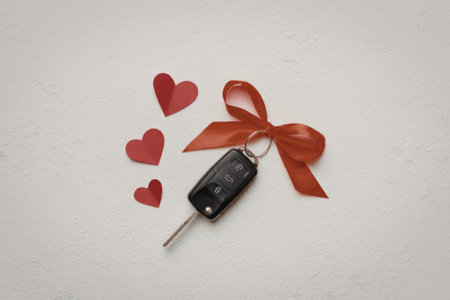 A car key with a red ribbon and three small red hearts on a white background