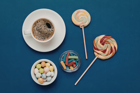 A vibrant arrangement of colorful sweets and a cup of coffee on a blue background, featuring lollipops, gummy candies, and coffee.