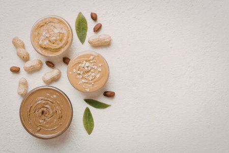 A visually appealing arrangement of peanut butter, peanuts, and leaves on a clean white background, showcasing a healthy snack option.