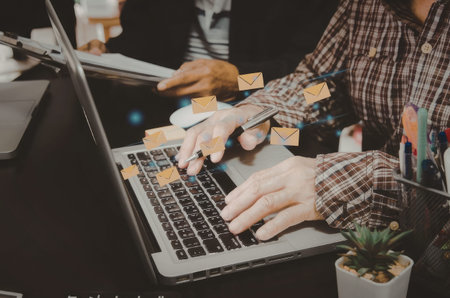 A person is working on a laptop with sticky notes on the keyboard and screen. The individual is wearing a plaid shirt and has a plant and pens nearby.