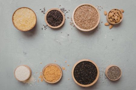An arrangement of various spices and herbs in small wooden bowls on a grey surface
